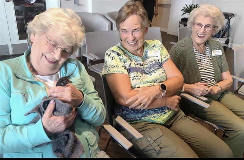 Senior women seated together smiling while holding a bird