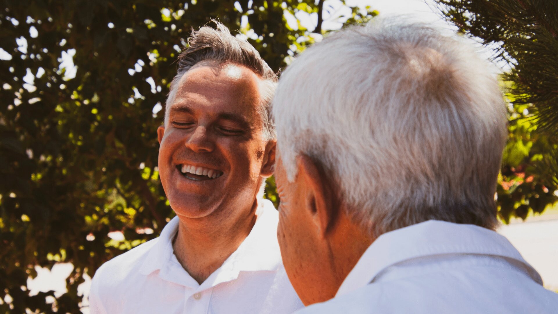 Two elderly people sitting under trees and smiling