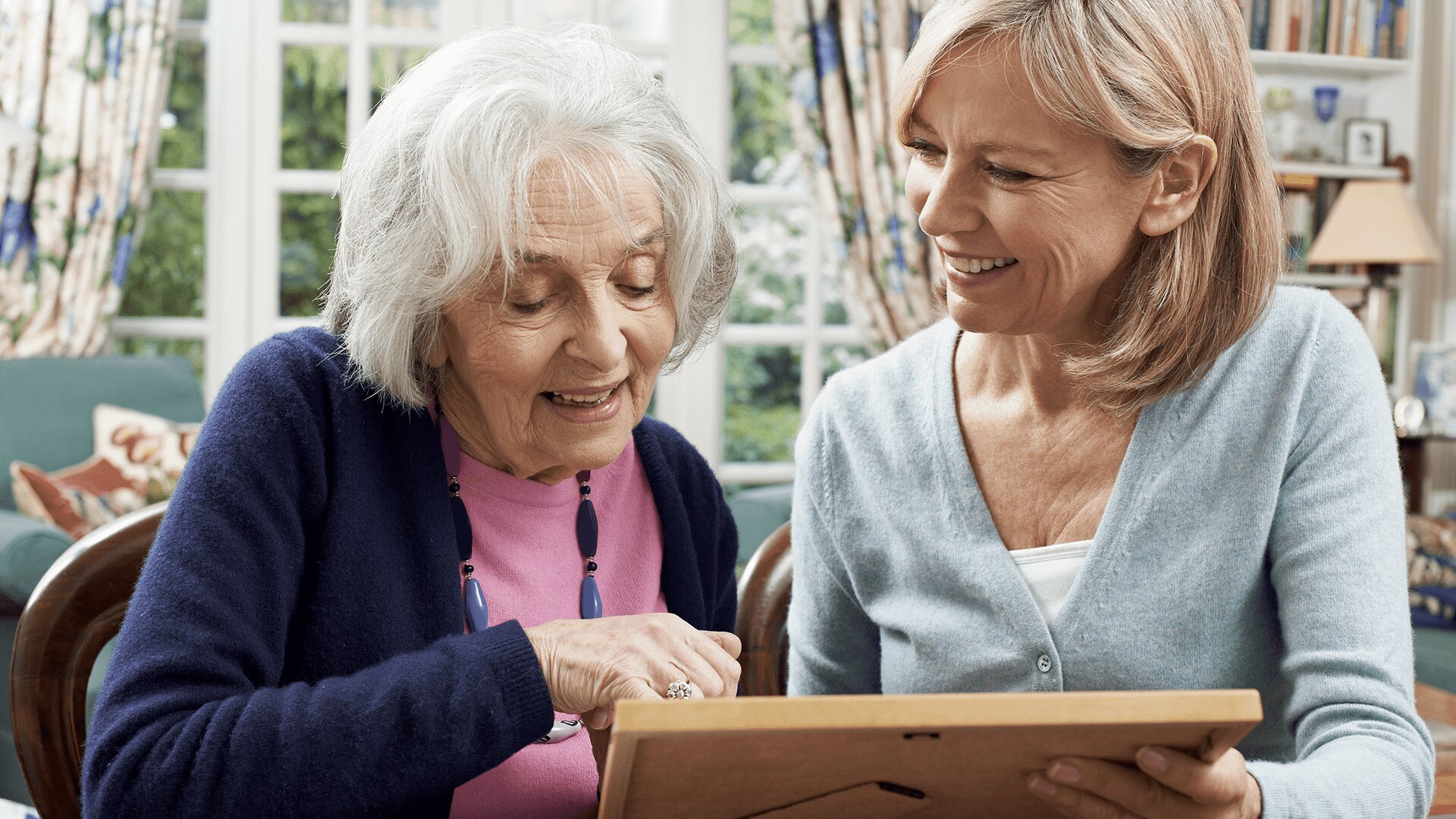 A senior woman looking at a photo with a middle-aged woman