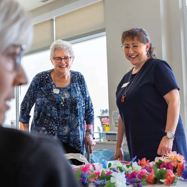 A staff member smiling alongside a senior with multiple flowers in front of them.