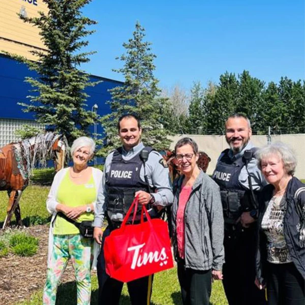 Three seniors taking a photo with two police officers. The one policeman is holding a bag of Tim Horton's doughnuts.