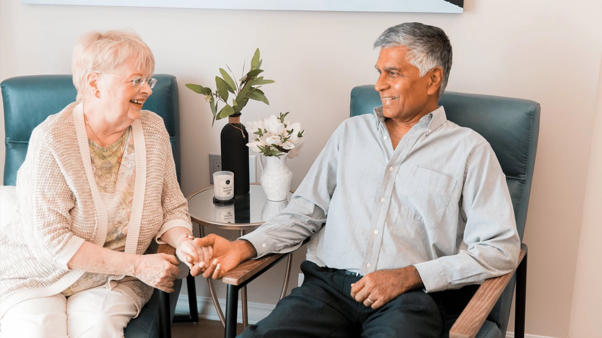 A senior couple smiling and sitting together while holding their hands at Aster Gardens