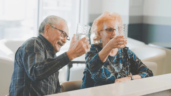 A happy elderly couple toasting at Aster Gardens Dining area