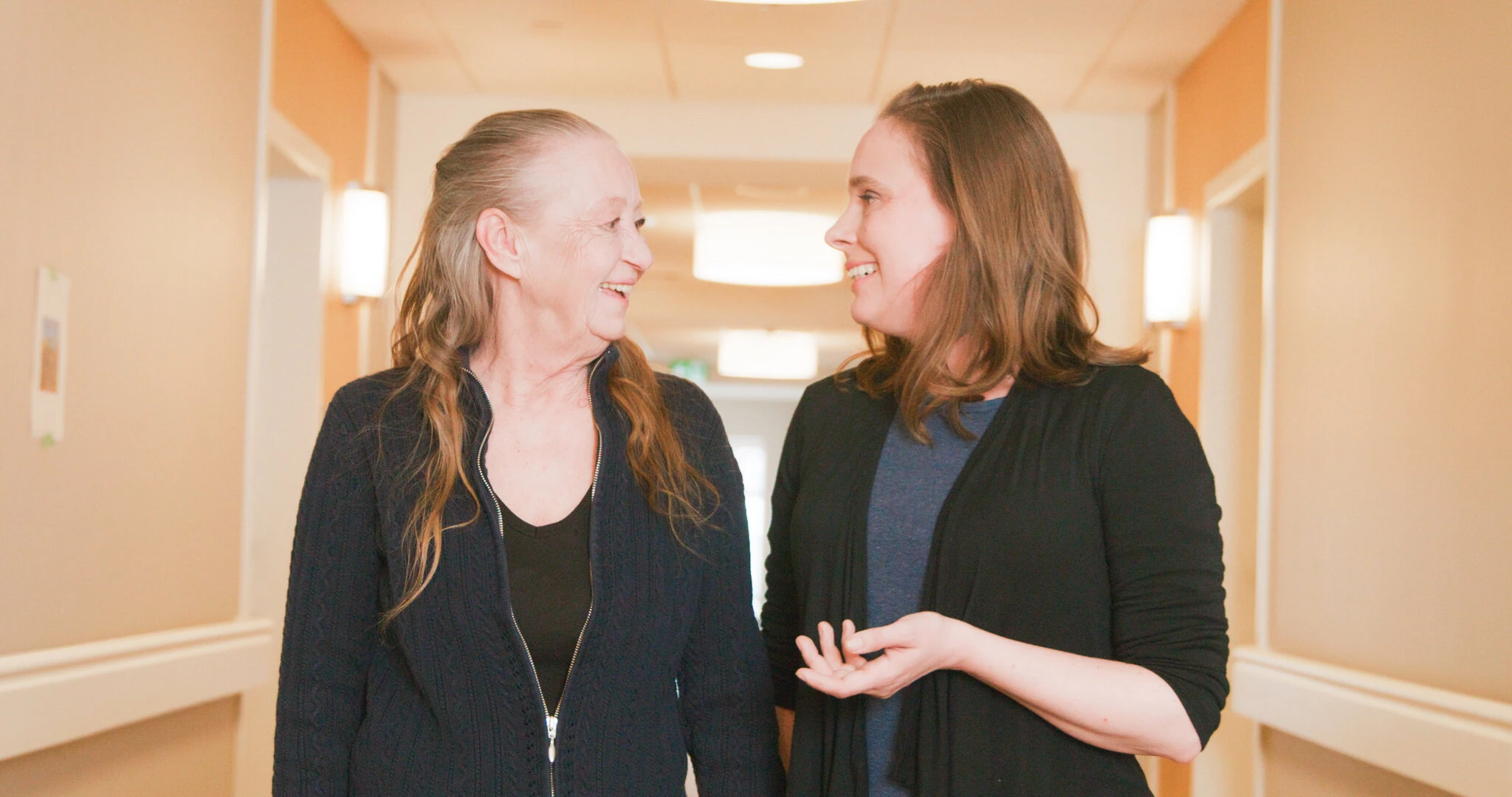 An elderly lady talking with a young woman while walking in corridors at Aster gardens