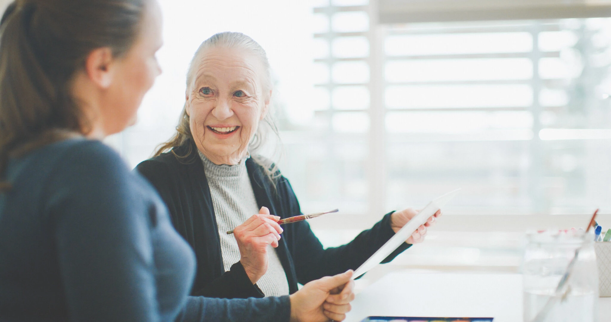 An elderly lady doing painting and showing to a young lady at AG