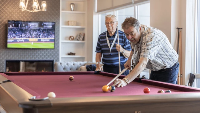 Two senior men playing pool and watching sports on tv