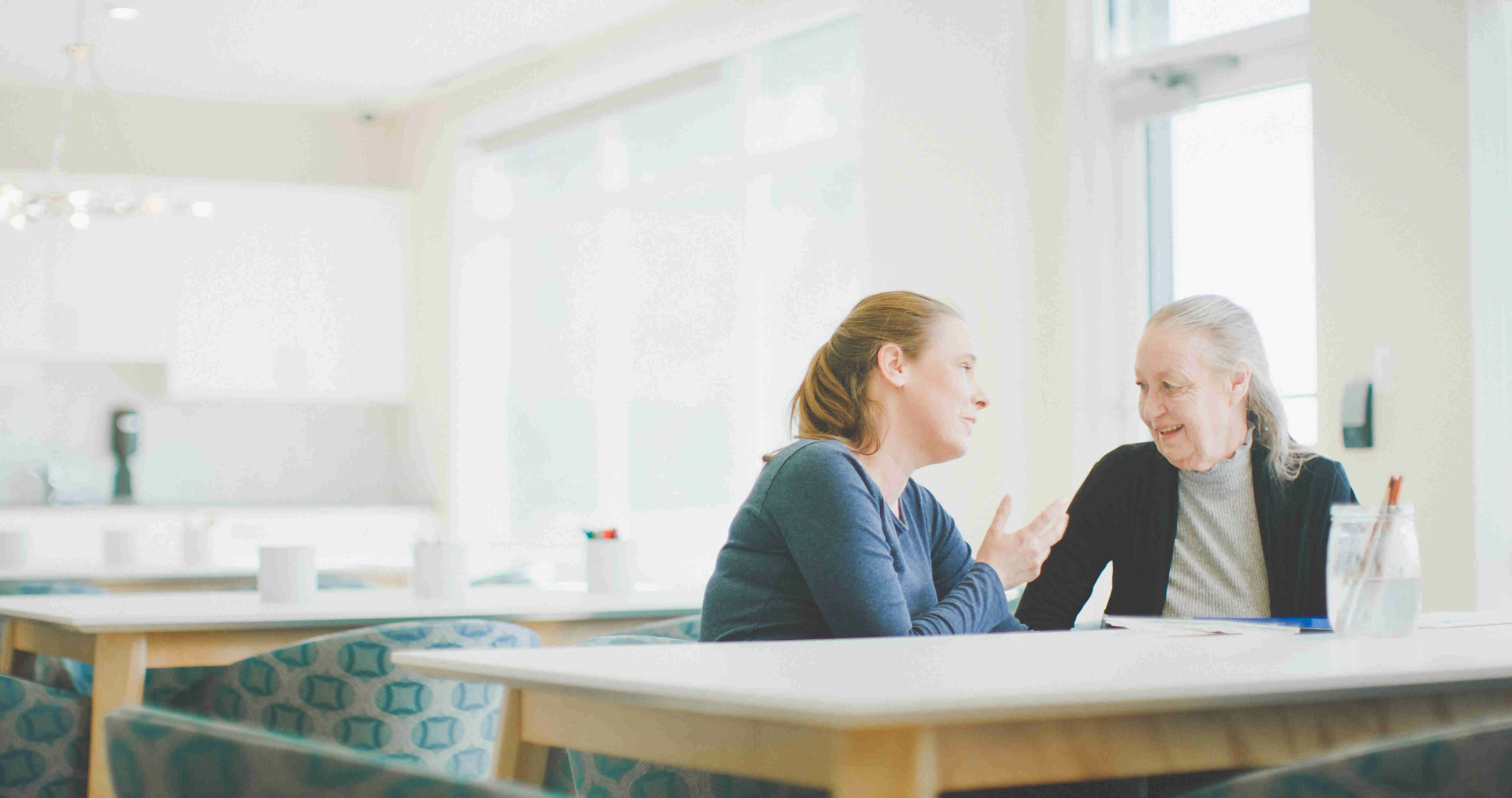 A senior woman talking to a younger woman at a table