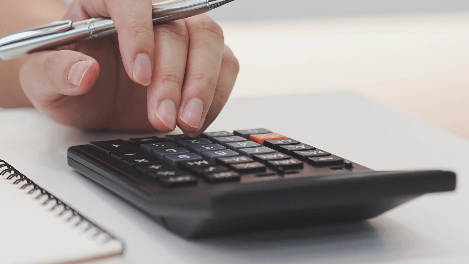 A hand holding a pen and typing on a calculator