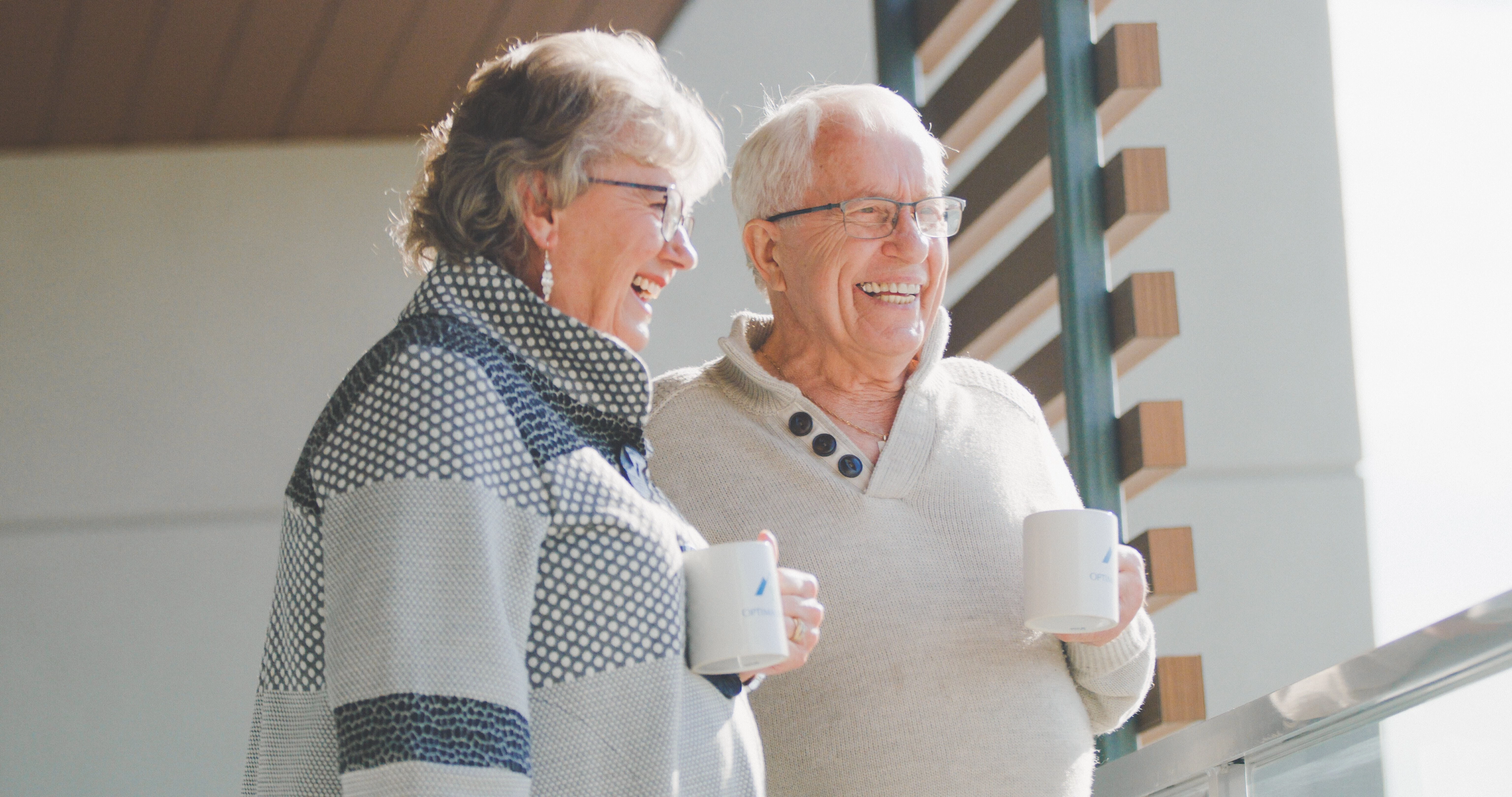 A happy elderly couple enjoying coffee while standing at the balcony