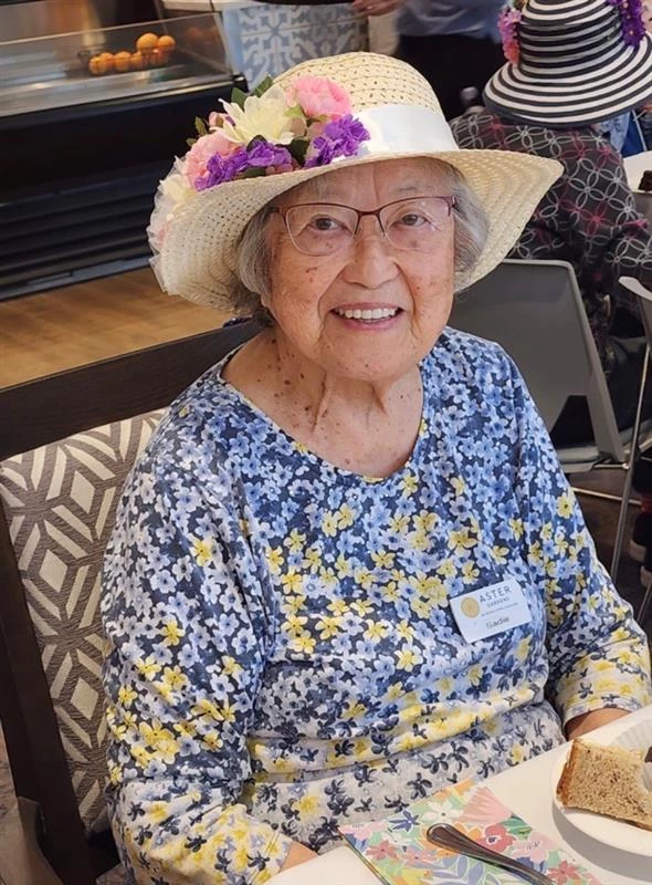 Senior woman sitting in a floral dress with a sun hat on.